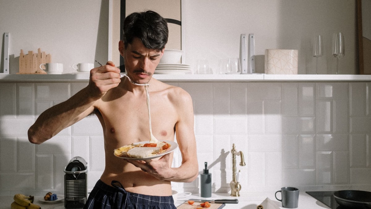 Young man enjoying a breakfast omelette in a sunlit kitchen setting.